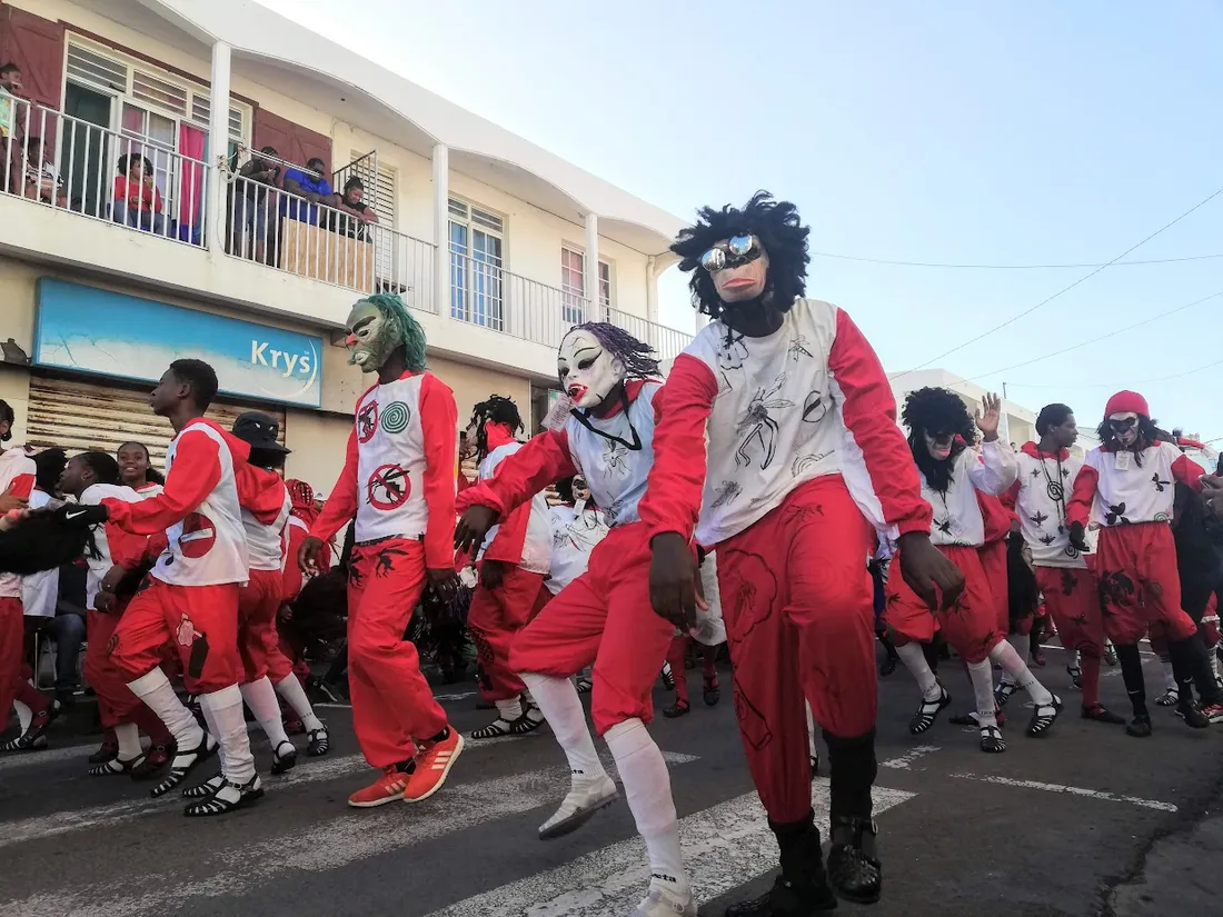 Groupe de carnaval masqué en costumes rouges et blancs dansant dans une rue du Moule lors du carnaval de Guadeloupe