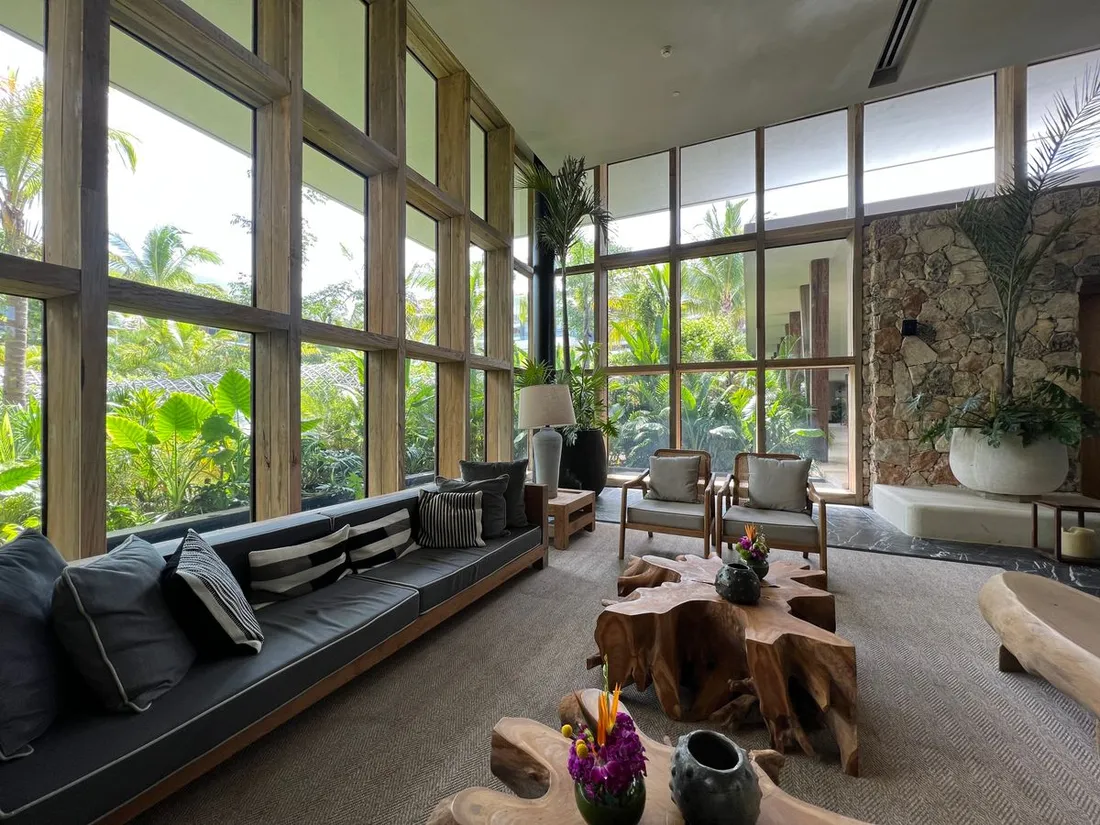 Salon meuble d'un logement de location avec baies vitrees ouvertes sur la vegetation tropicale