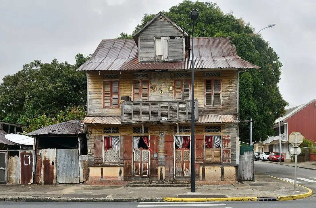 Ancienne maison créole en bois très dégradée à l'angle d'une rue de Cayenne en Guyane, illustrant les besoins d'entretien