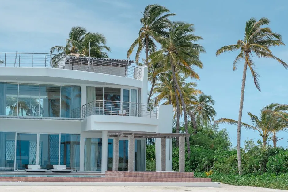 Villa de location de vacances moderne aux baies vitrées entourée de cocotiers en bord de mer, illustrant un meublé de tourisme classé