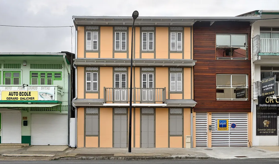 Maison créole de plusieurs étages à Cayenne en Guyane portant un panneau de location, illustrant un bien meublé proposé à la location