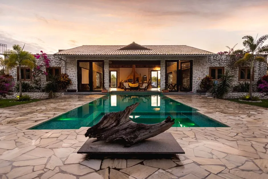 Villa tropicale haut de gamme en pierre avec grande piscine au coucher du soleil, jardin et terrasse en dallage
