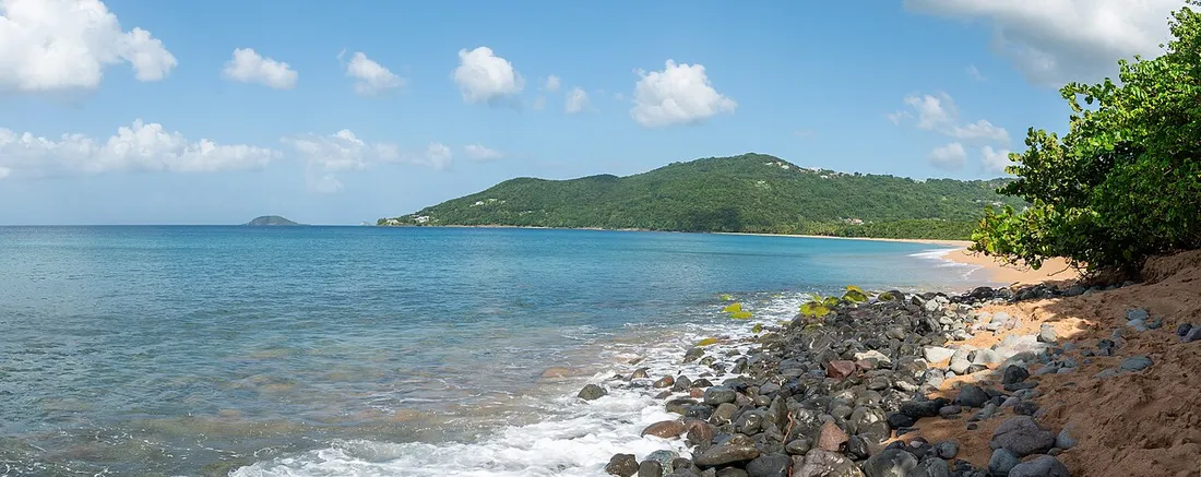 Plage de Grande Anse à Deshaies en Guadeloupe, sable doré bordé de collines boisées et eaux turquoise des Caraïbes