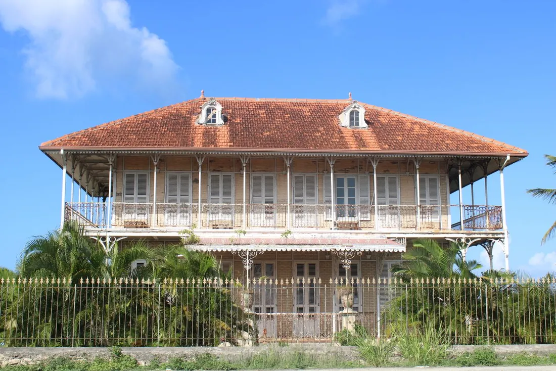 Maison créole coloniale traditionnelle en Guadeloupe, toit de tuiles rouges et large véranda, illustrant un meublé de tourisme