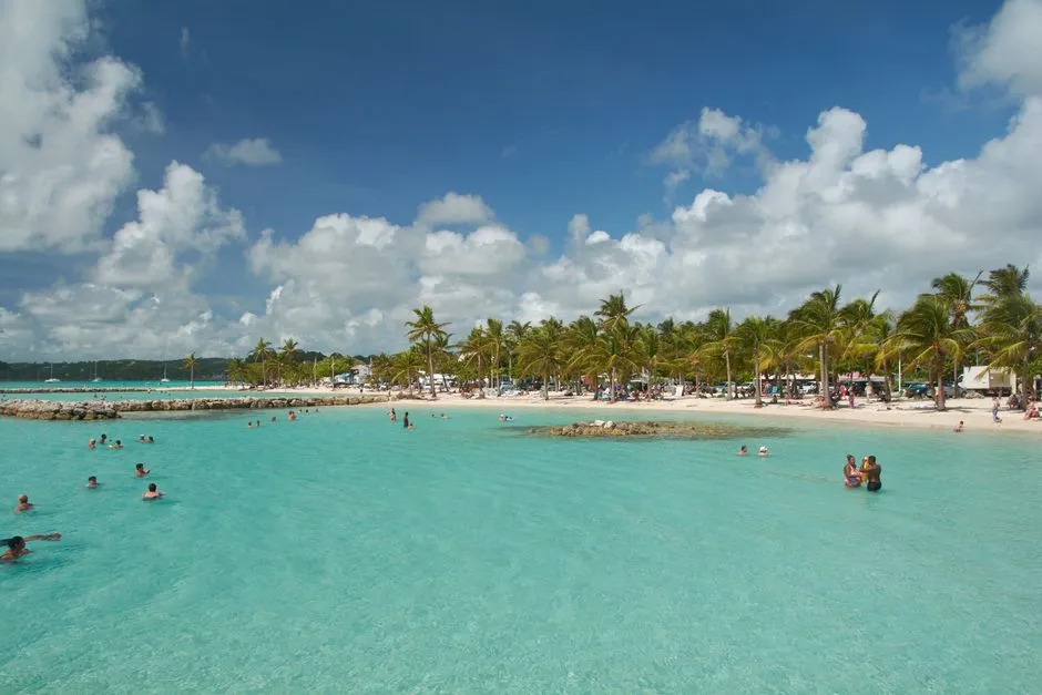 Lagon peu profond et calme d'une plage de Sainte-Anne en Guadeloupe ou des familles se baignent dans une eau turquoise abritee par une barriere rocheuse
