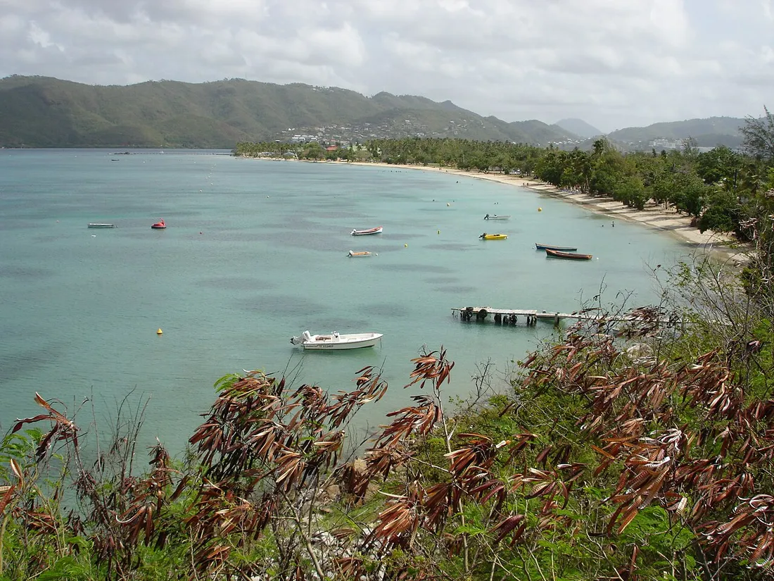 Plage de Sainte-Anne en Martinique : baie aux eaux turquoise bordée de sable et de collines verdoyantes, avec des barques au mouillage