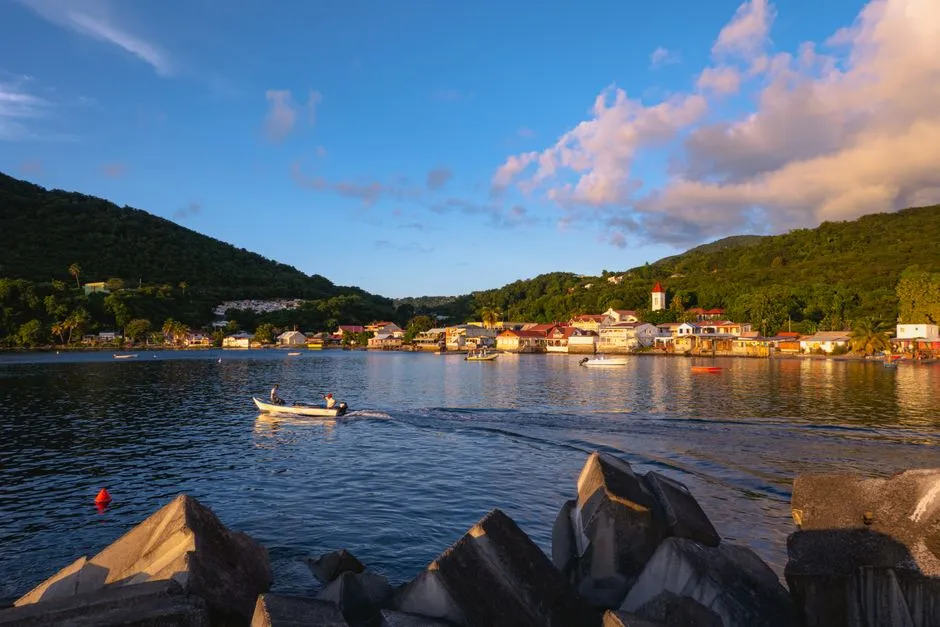Village côtier de Deshaies en Guadeloupe au coucher du soleil, maisons en bord de baie et petit bateau, illustrant les biens en location dans l'île