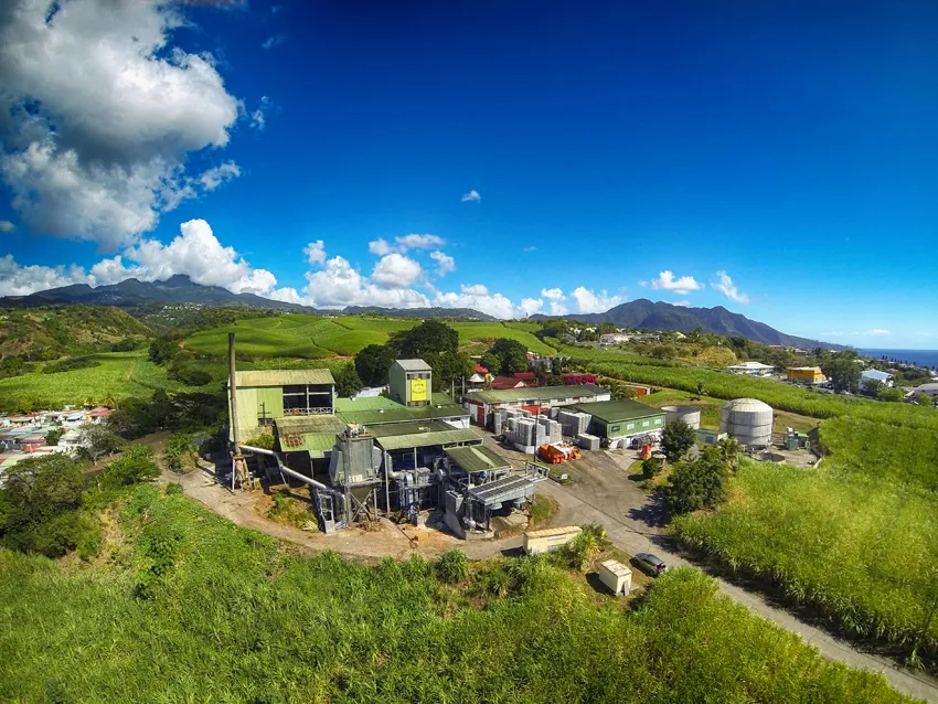 Vue aérienne de la distillerie de rhum agricole Bologne en Guadeloupe, entourée de champs de canne à sucre au pied des montagnes de Basse-Terre