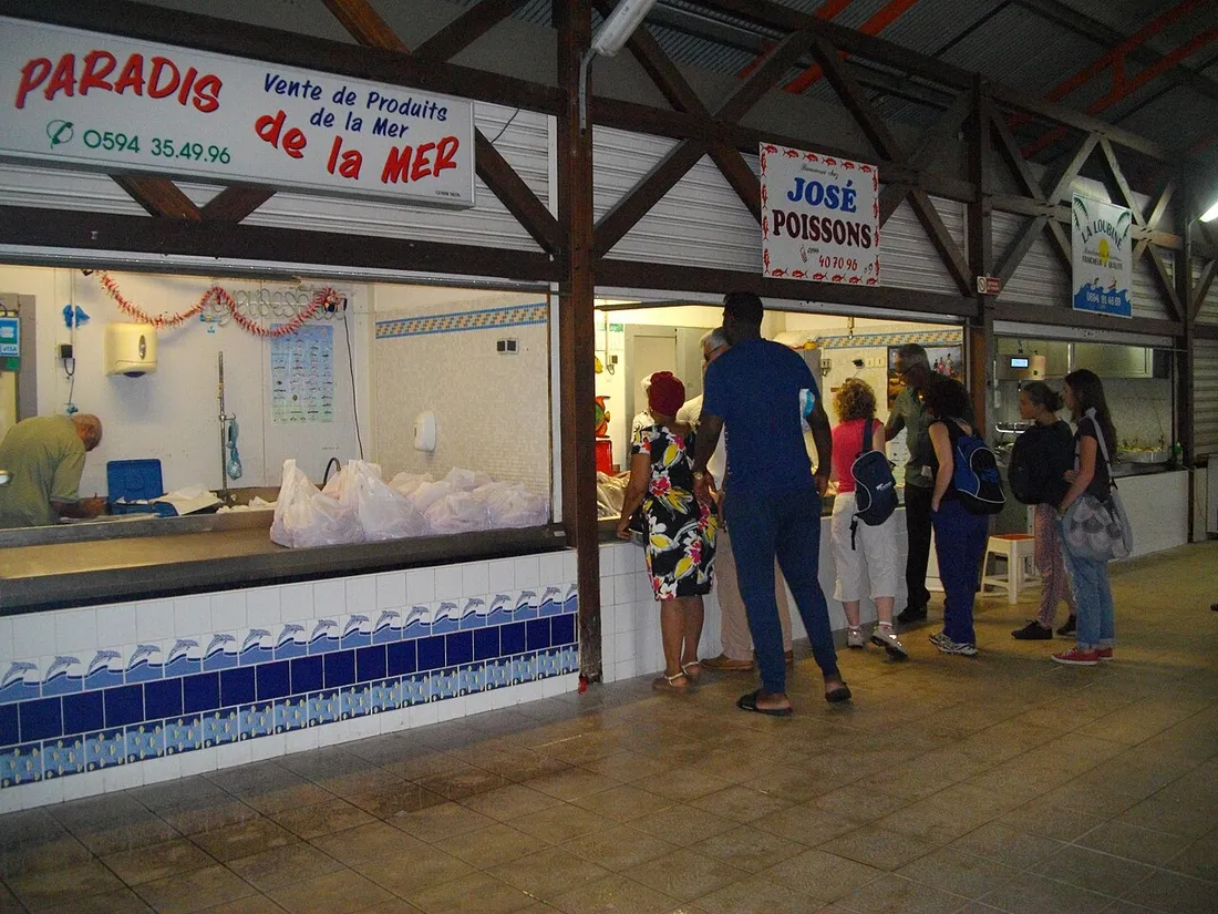 Étal de produits de la mer au marché d'intérêt régional de Cayenne, avec poissonniers et clients sous la halle