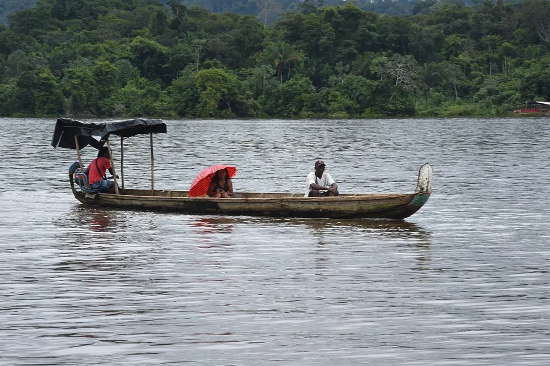 Excursion en pirogue traditionnelle avec passagers sur le fleuve Maroni en Guyane, forêt dense en arrière-plan
