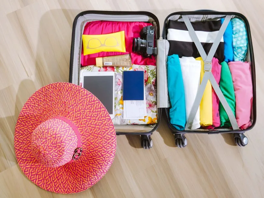 Valise ouverte soigneusement remplie pour la Martinique : vêtements d'été colorés, maillot de bain, lunettes de soleil, chapeau de paille, passeport et appareil photo