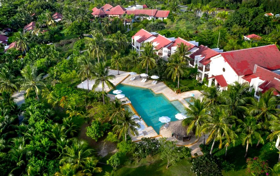 Vue aerienne d'une villa tropicale avec piscine entouree de cocotiers, evoquant une location proche plage