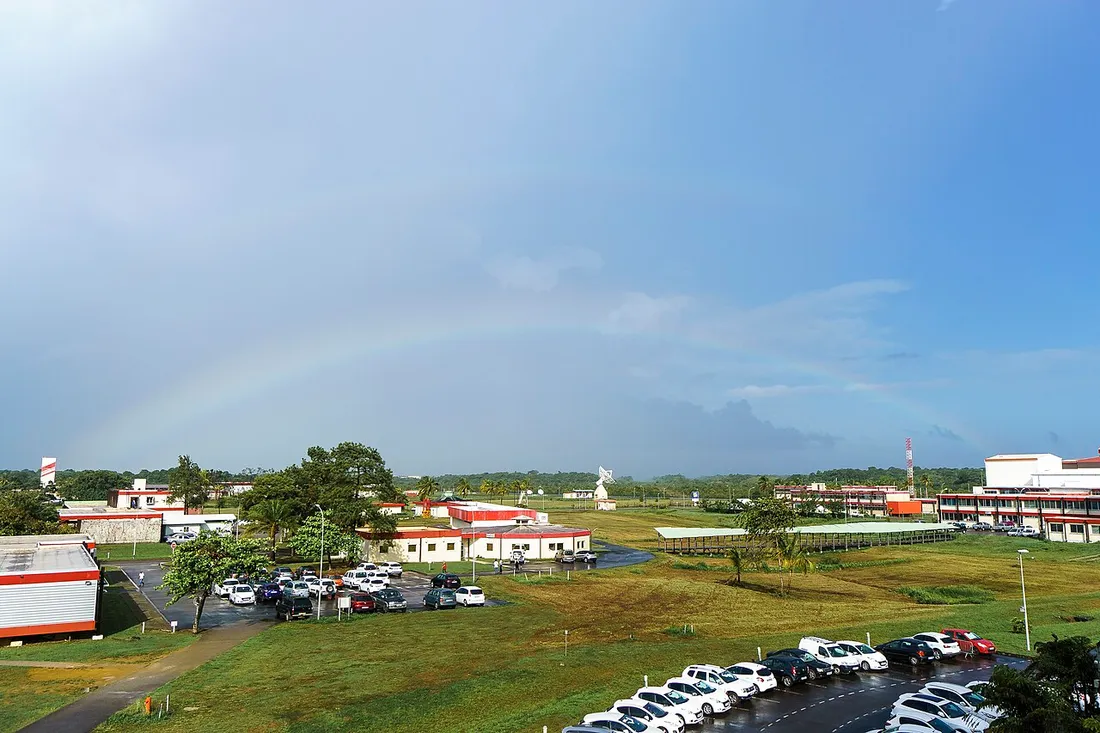 Vue du Centre Spatial Guyanais à Kourou avec ses bâtiments, une antenne paraboliques de suivi et un arc-en-ciel dans le ciel guyanais